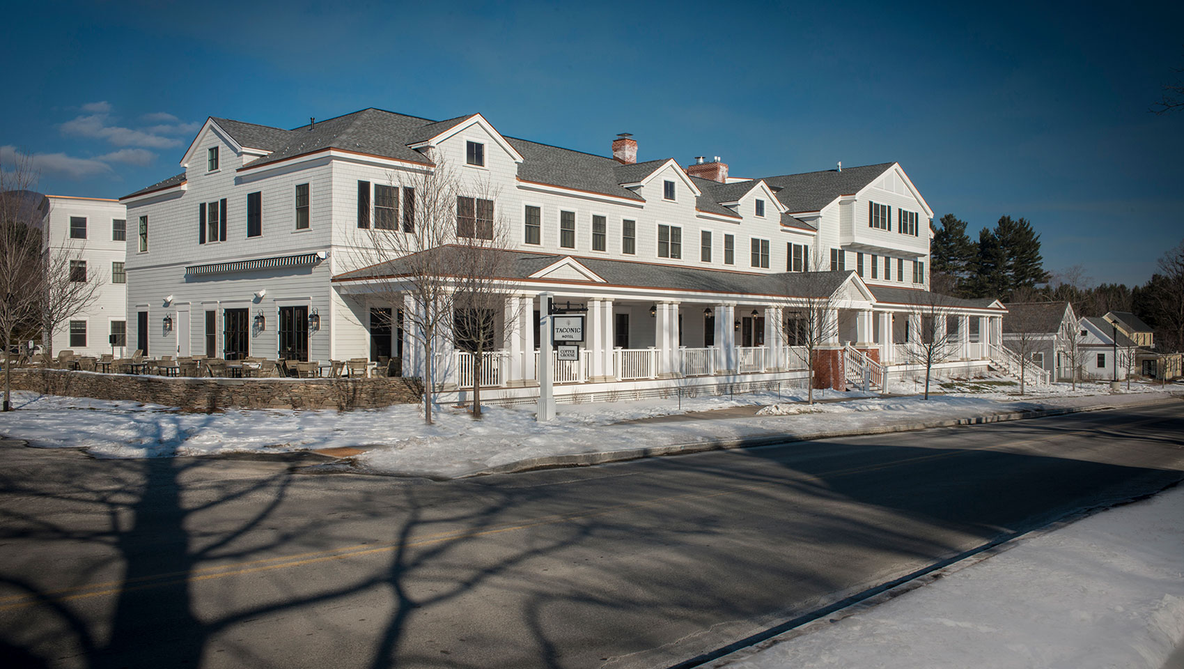 The white Taconic Hotel stands in a snowy landscape with tree shadows on a street